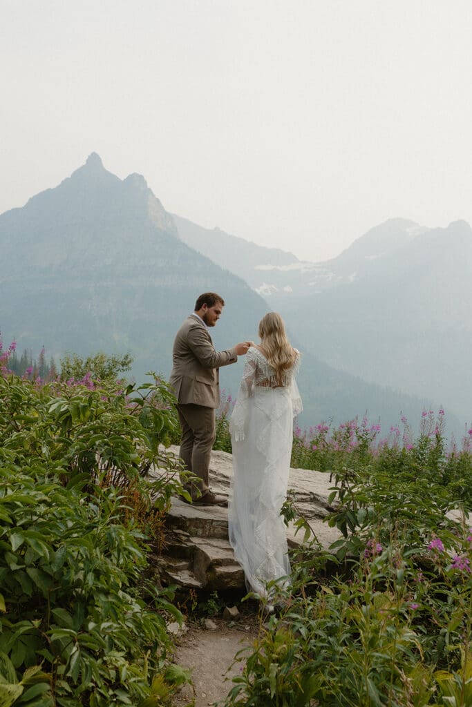 Groom helping bride onto a rock in the mountains.