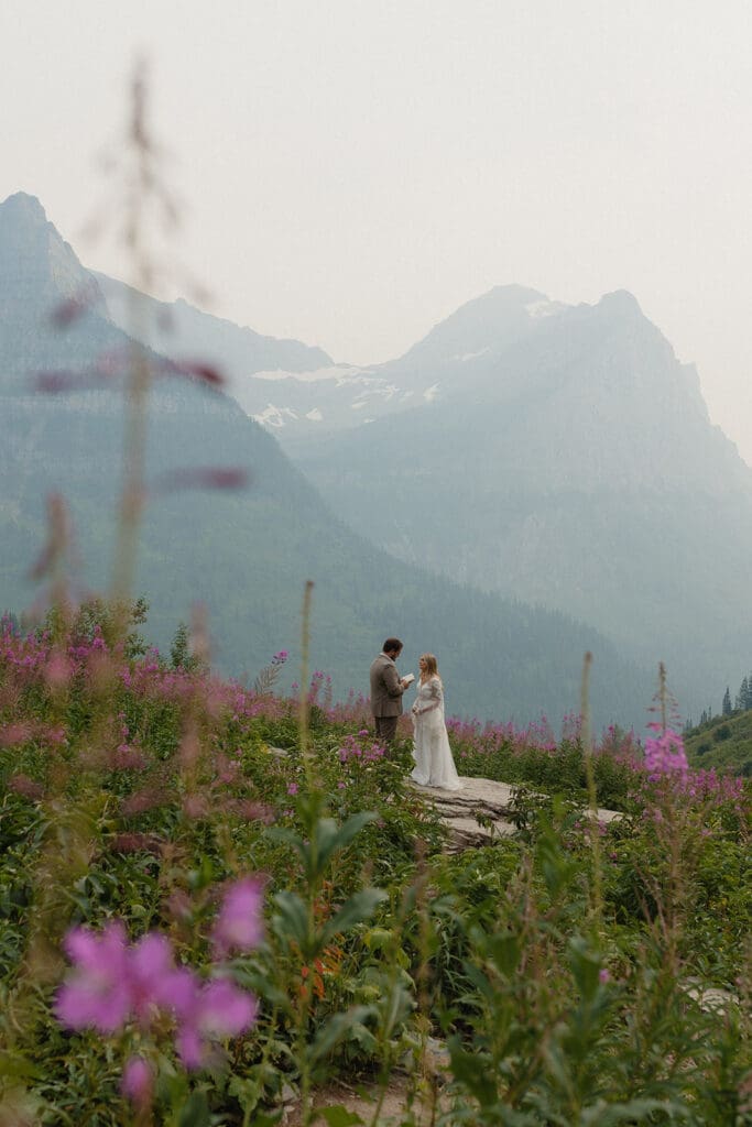 Bride and groom from a distance exchanging vows on a rock in the mountains.