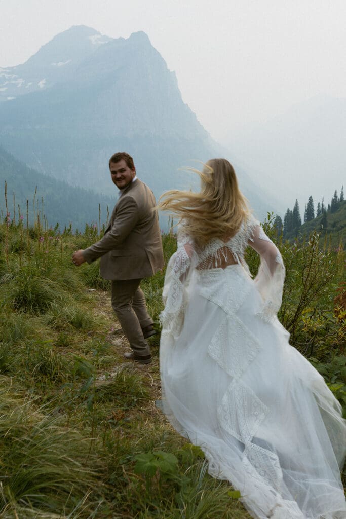 Bride and groom running in a field with mountains in background.