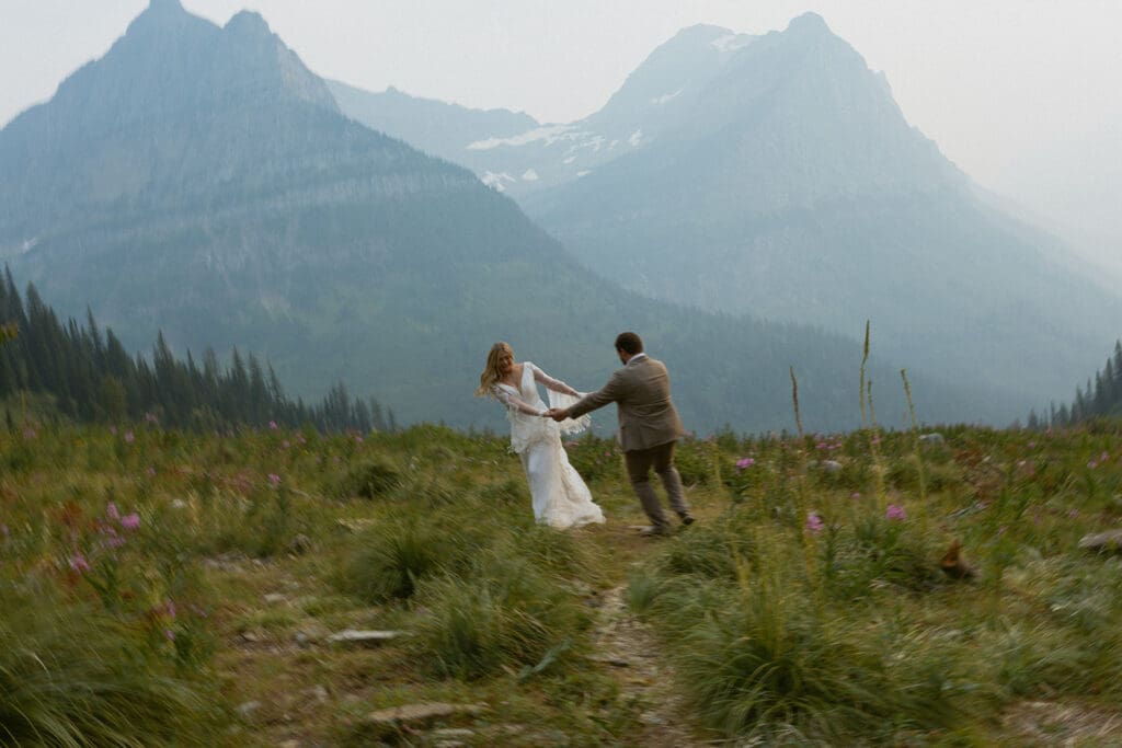Bride and groom running in a field with mountains in background.